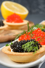 tartlets with red and black caviar on a white plate with lemon on a gray background. Close-up