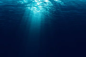 Poster perfect naadloos van diepblauwe oceaangolven van onderwaterachtergrond met stromende microdeeltjes, lichtstralen die er doorheen schijnen © donfiore