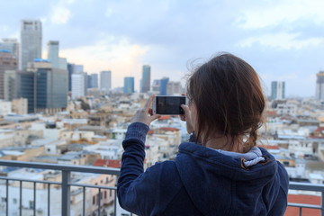 Tourist woman taking picture of Tel Aviv skyline panorama with smartphone in the evening, Israel