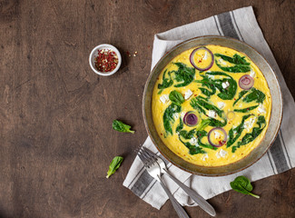 omelet with spinach and feta cheese in an iron pan on a wooden, rustic background. Top view. copy space
