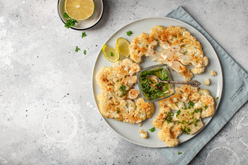 baked cauliflower steaks with pesto. light background. top view. copy space