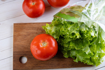 Red tomatoes with water droplets and green lettuce are on a wooden board.