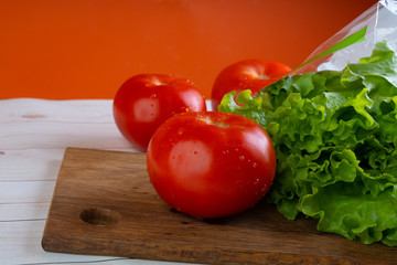 Red tomatoes with water droplets and green lettuce are on a wooden board.