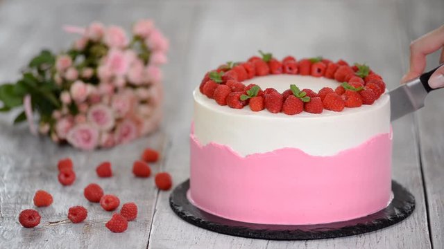 Womens hands cut a delicious summer cake with raspberry.