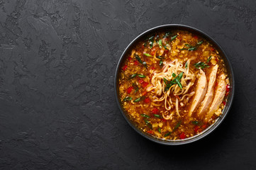 Chicken Manchow Soup in black bowl at dark slate background. Chicken Manchow Soup is indo-chinese cuisine dish with bell peppers, cabbage, carrot, noodles, chilli, soy sauce, green onion and chicken 