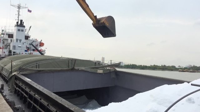 Large yellow scoop Are scooping the white Urea chemical fertilizer From a pontoon boat to unload