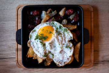 Fried egg with beautiful yellow yolk on baked potato with bacon and sausages - cooked at home in the kitchen