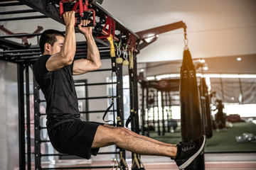 Fitness man hanging on horizontal bar performing legs raises, in the gym