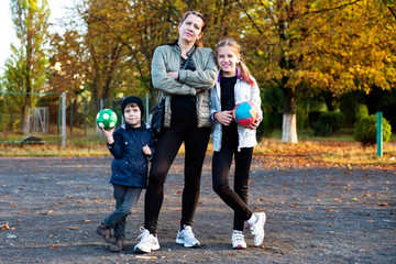 Fototapeta premium Happy mom has fun playing with her children on the playground. They stopped to rest, the children holding a balls