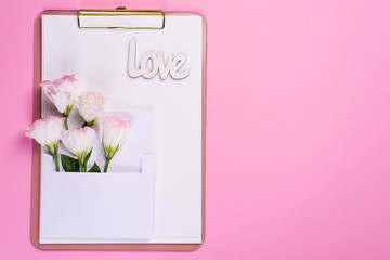 Minimal composition with a Eustoma flowers in an envelope on clipboard on a pink background, top view. Valentines day, birthday, mother or wedding greeting card