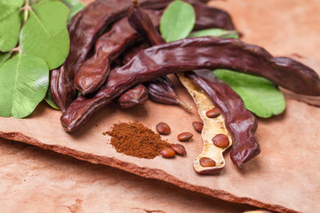 Carob. Organic carob pods with seeds and leaves on tree bark table. Healthy eating, food background.