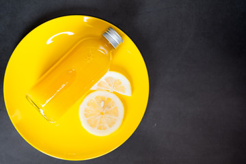 Fresh orange juice in bottle and ripe juicy lemons slice on yellow dish