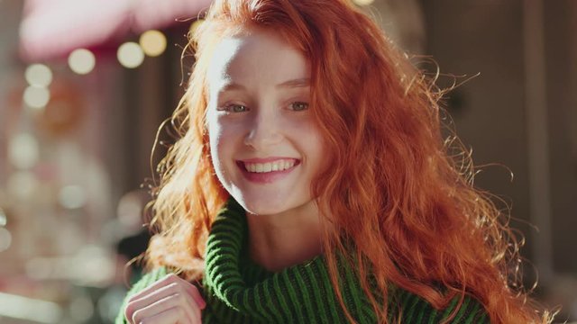 Portrait of charming adorable ginger girl in green outfit smiling with joy staying in european city center at afternoon sunlight.