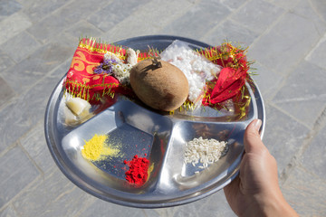 Hand holding offerings to Shiva in metal plate - coconut, trident, turmeric, flowers. Close-up,...