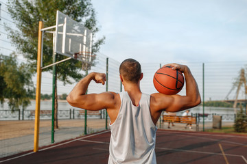 Male basketball player with ball shows his muscles