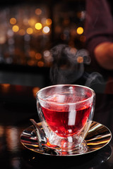 Beautiful transparent cup with red fruit tea on a shiny dark table on a blurred bar background. Close-up. Space