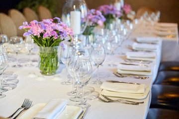 Table setting for guests in a restaurant, on the table forks and glasses for wine - flowers in a vase and a candle on the table