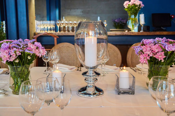 Table setting for guests in a restaurant, on the table forks and glasses for wine - flowers in a vase and a candle on the table
