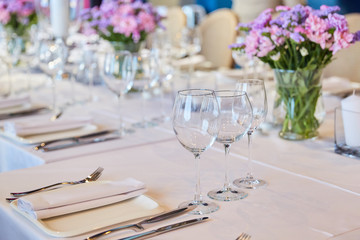 Table setting for guests in a restaurant, on the table forks and glasses for wine - flowers in a vase and a candle on the table