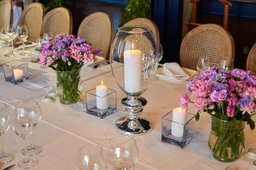 Table setting for guests in a restaurant, on the table forks and glasses for wine - flowers in a vase and a candle on the table