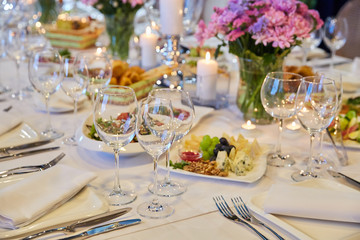 Table setting for guests in a restaurant, on the table forks and glasses for wine - flowers in a...