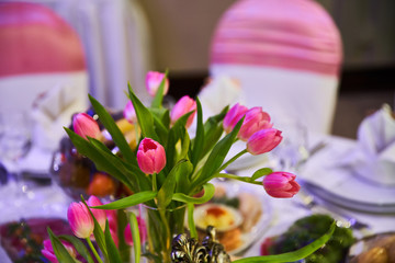 A bouquet of red tulips is on the wedding table in a glass vase