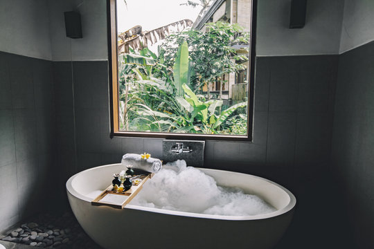 Bath With Foam Is Filling With Water, Beauty Products On Bathtub.