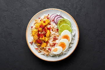 Nan Gyi Thoke in black bowl at dark slate background. Nan gyi Thohk is popular burmese cuisine dish with rice noodles, chicken breasts with spices, eggs, peanuts, lime and red onion. Top view