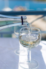 Waiter pouring white wine in glass on terrace table with sea view