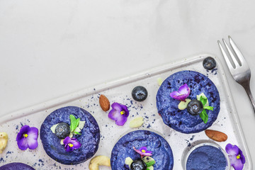 raw blue vegan cakes with fresh berries, mint, nuts and edible flowers. healthy vegan food concept. top view