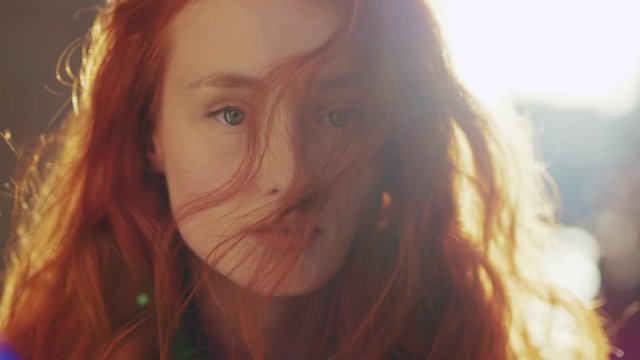 Attractive cute redhead european woman looking straight at camera with gorgeous hair blowing in the wind outdoors. Beauty portrait. Close-up.