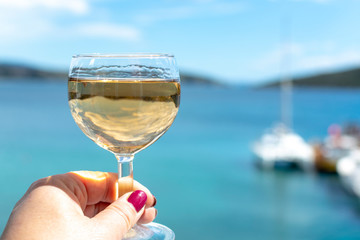 hand with glass of white wine served outside on balcony with sea view
