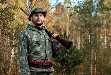 Fototapeta premium Hunter man in camouflage with a gun during the hunt in search of wild birds or game on the background of the autumn forest. Autumn hunting season. The concept of a hobby, killing.