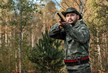 Obraz premium Hunter man in camouflage with a gun during the hunt in search of wild birds or game on the background of the autumn forest. Autumn hunting season. The concept of a hobby, killing.