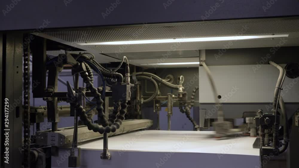 Poster a static footage showing a machine with stack of large sheets of papers, being printed at the printi
