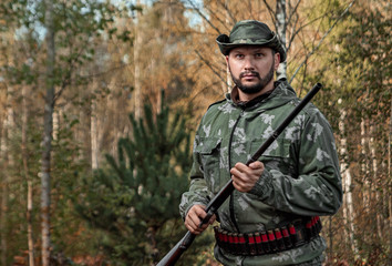 Naklejka premium Hunter man in camouflage with a gun during the hunt in search of wild birds or game on the background of the autumn forest. Autumn hunting season. The concept of a hobby, killing.