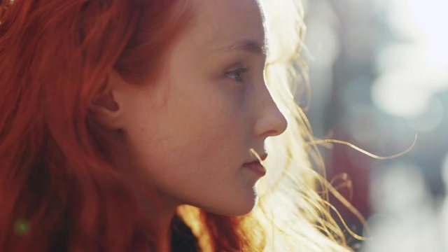 Beauty profile of pretty dreamy red-head millennial girl looking straight with wind blowing gently in sunshines outdoor. Close-up.