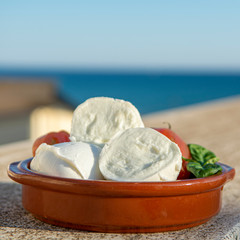 Italian mozzarella soft cheese in balls served with tomatoes and fresh basil outdoor with blue sea view