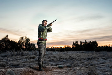 Obraz premium Myśliwy mężczyzna w kamuflażu z bronią podczas polowania w poszukiwaniu dzikiego ptactwa lub zwierzyny łownej na pięknym zachodzie słońca. Pojęcie hobby, zabijanie.