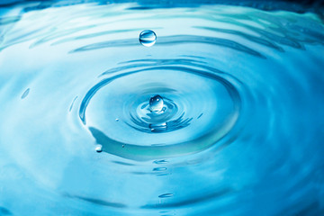 Naklejka na ściany i meble Close up blue water drop splash on water surface.
