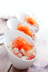 Fototapeta na wymiar Salad with seafood and red caviar in portioned bowls on a wooden table, selective focus