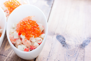 Fototapeta na wymiar Salad with shrimp, squid, crab sticks and red caviar in portioned eggs on a wooden table, horizontal, copy space