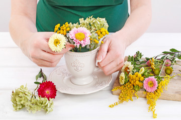 Woman shows how to make floral arrangement with summer flowers inside a ceramic cup