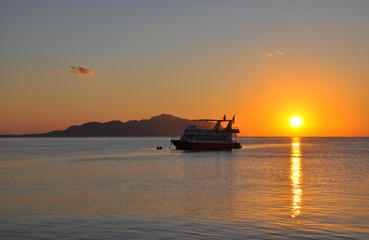 Obraz premium Boat on sunrise in the sea with flags with the island on the background