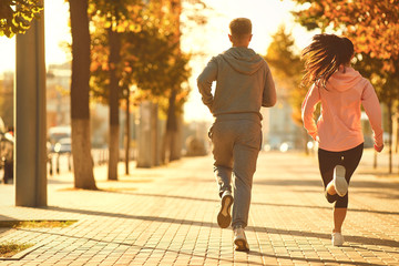 A man and a woman are running along the city street in the morning.