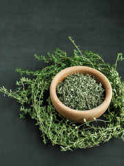 Wooden bowl of dry thyme (thymus serpyllum) on black background.