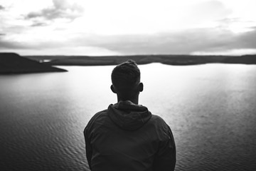 Loneliness concept. Hipster traveler in windbreaker standing alone on top of rock mountain with...
