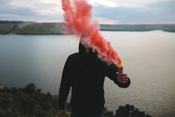 Ultras hooligan holding red smoke bomb in hand, standing on top of rock mountain with amazing view...