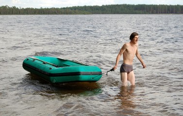 Naked happy young man with rubber green inflatable boat in the lake 