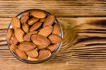 Glass bowl with the peeled almond nuts on wooden table. Top view